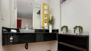 A bathroom with a black countertop, a white sink, a mirror, a towel rack, and a small plant.