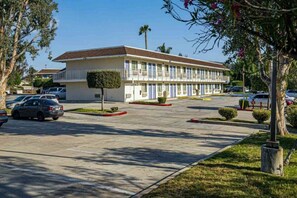 A motel with a central parking lot, a row of single-story buildings with balconies, and a small tree in the foreground. - 1 Queen Bed | Premium, Mini Fridge (Temecula)