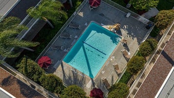 An aerial view of a swimming pool surrounded by lounge chairs and umbrellas, with a fence enclosing the area.