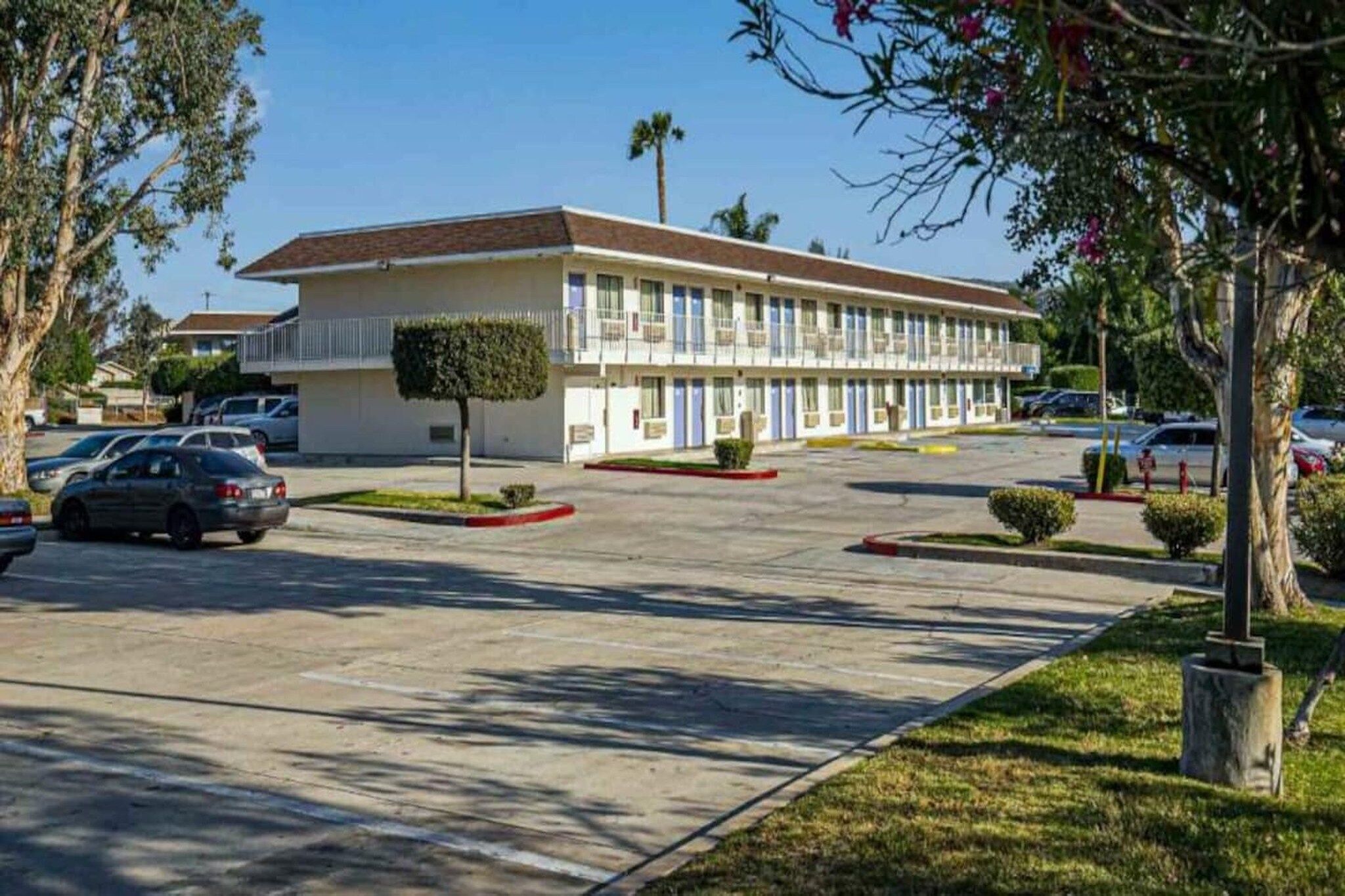 A motel with a central parking lot, a small tree, and a clear sky.
