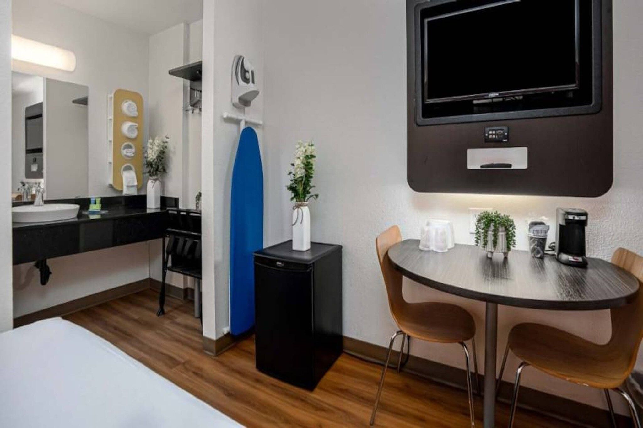 A hotel room with a bed, a desk with a chair, a coffee machine, a TV, and a small refrigerator.