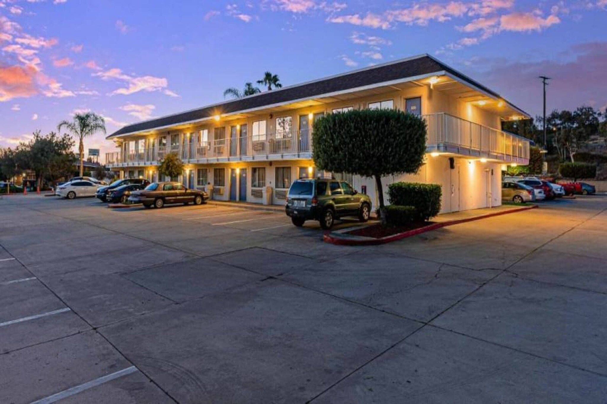 A motel with a parking lot, multiple cars, and a well-lit building at dusk.