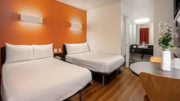 A hotel room with two beds, a wooden floor, a round table with chairs, and a bathroom visible through an open door.