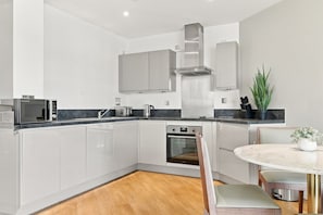 Een moderne keuken met witte kasten, een roestvrijstalen afzuigkap, een inbouwoven en een ronde eettafel met een bank.