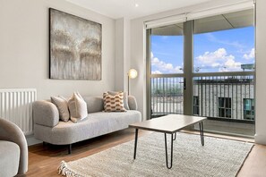 A modern living room with a grey sofa, a coffee table, and a large window offering a view of a building. - 2 Bed 2 Bath Willesden Junction New furniture (Greater London)