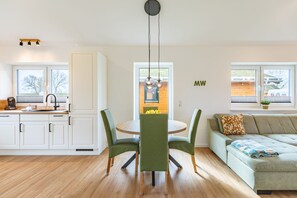 Eine moderne Küche mit weißen Schränken, ein Essbereich mit grünen Stühlen und ein Wohnzimmer mit einem grünen Sofa.