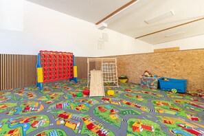 Ein Spielzimmer mit einer bunten Spielmatte, einer Kletterlandschaft und Aufbewahrungsboxen.