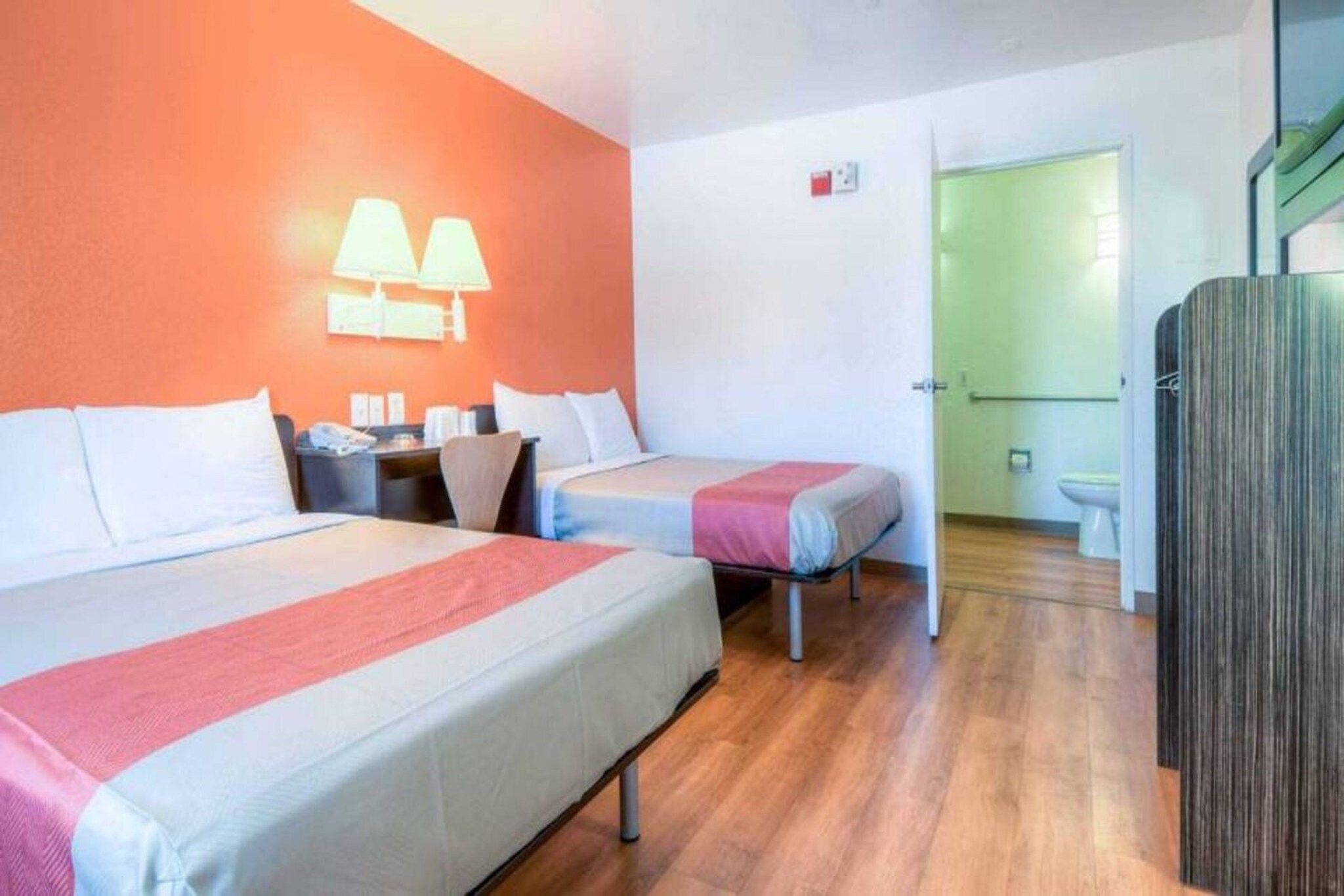 A hotel room with two beds, a desk, a chair, a lamp, and a wardrobe.