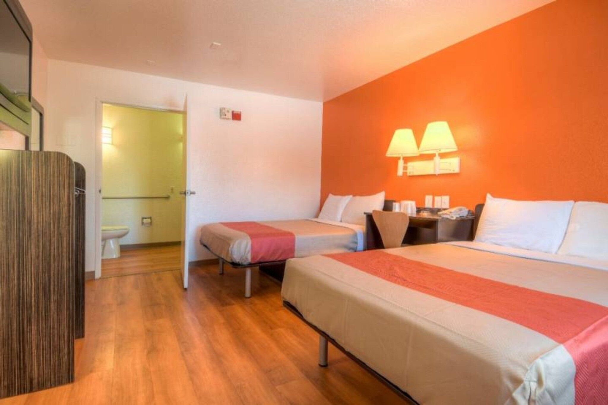 Habitación de hotel con dos camas, piso de madera y baño a la vista.