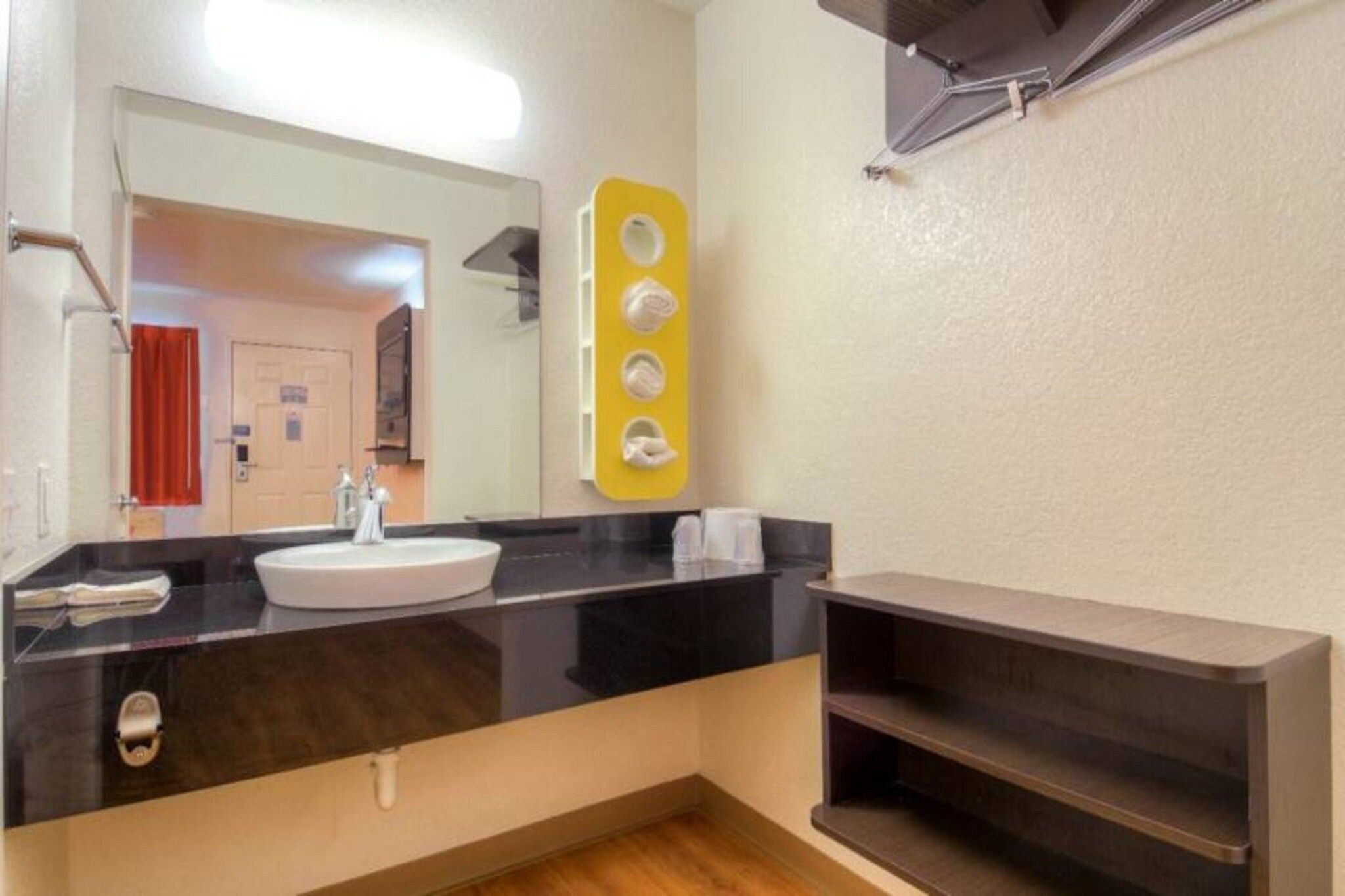 A bathroom with a sink, mirror, towel dispenser, and a shelf.