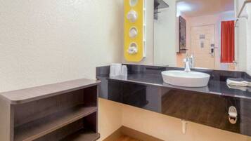 A bathroom with a black countertop, a white sink, and a mirror. There is a yellow soap dispenser holder on the wall.