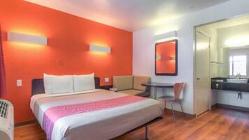 A hotel room with a bed, a desk, a chair, and a bathroom.