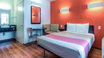 Une chambre d’hôtel comprenant un lit, un bureau, une chaise, une salle de bain et un mur d’accent de couleur rouge.