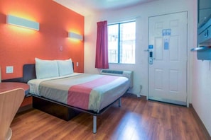 Een hotelkamer met een bed, een bureau, een raam met gordijnen en een deur.