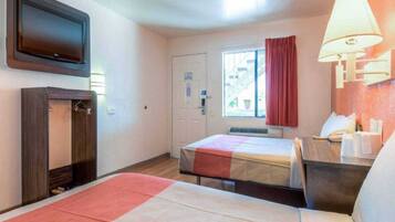 A hotel room with a bed, a desk, a television, a window with curtains, and a wall-mounted lamp.