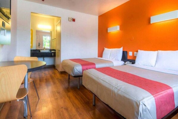 A hotel room with two beds, a small table, and a chair. - 2 Full Beds | ADA/Tub Non-smoking (Chula Vista)
