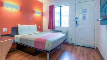 A hotel room with a bed, a desk, a window with curtains, and a door.