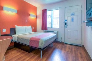 Ein Hotelzimmer mit einem Bett, einem Schreibtisch, einem Fenster mit Vorhängen und einer Tür.