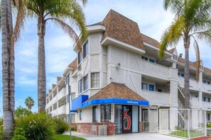 Ein mehrstöckiges Hotel mit flachem Dach, einer blauen Markise und einem gut sichtbaren Eingang mit einem 'welcome'-Schild.