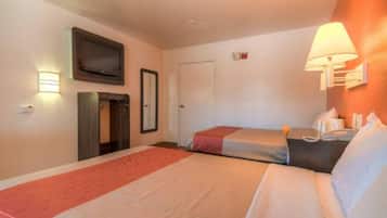 A hotel room with two beds, a television, a door, and a wall-mounted lamp.