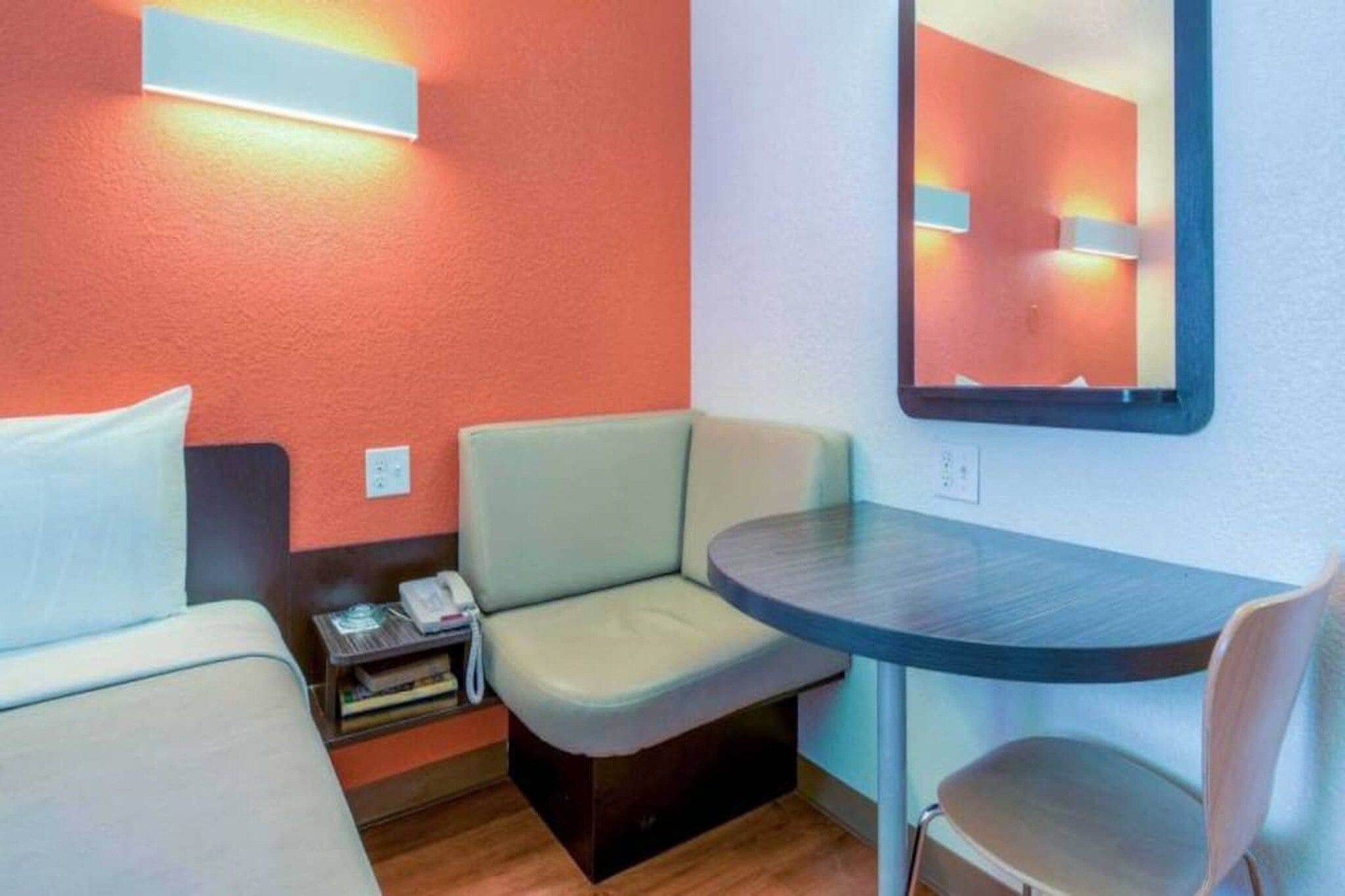 Une petite chambre d’hôtel avec deux lits, un bureau, une chaise, une table de chevet avec un téléphone et un miroir au mur.