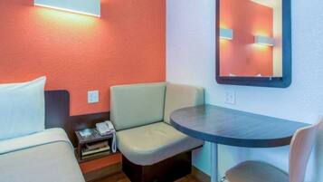 A small hotel room with two beds, a desk, a chair, a bedside table with a phone, and a mirror on the wall.