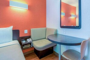 Ein kleines Hotelzimmer mit zwei Betten, einem Schreibtisch, einem Stuhl, einem Nachttisch mit Telefon und einem Spiegel an der Wand.