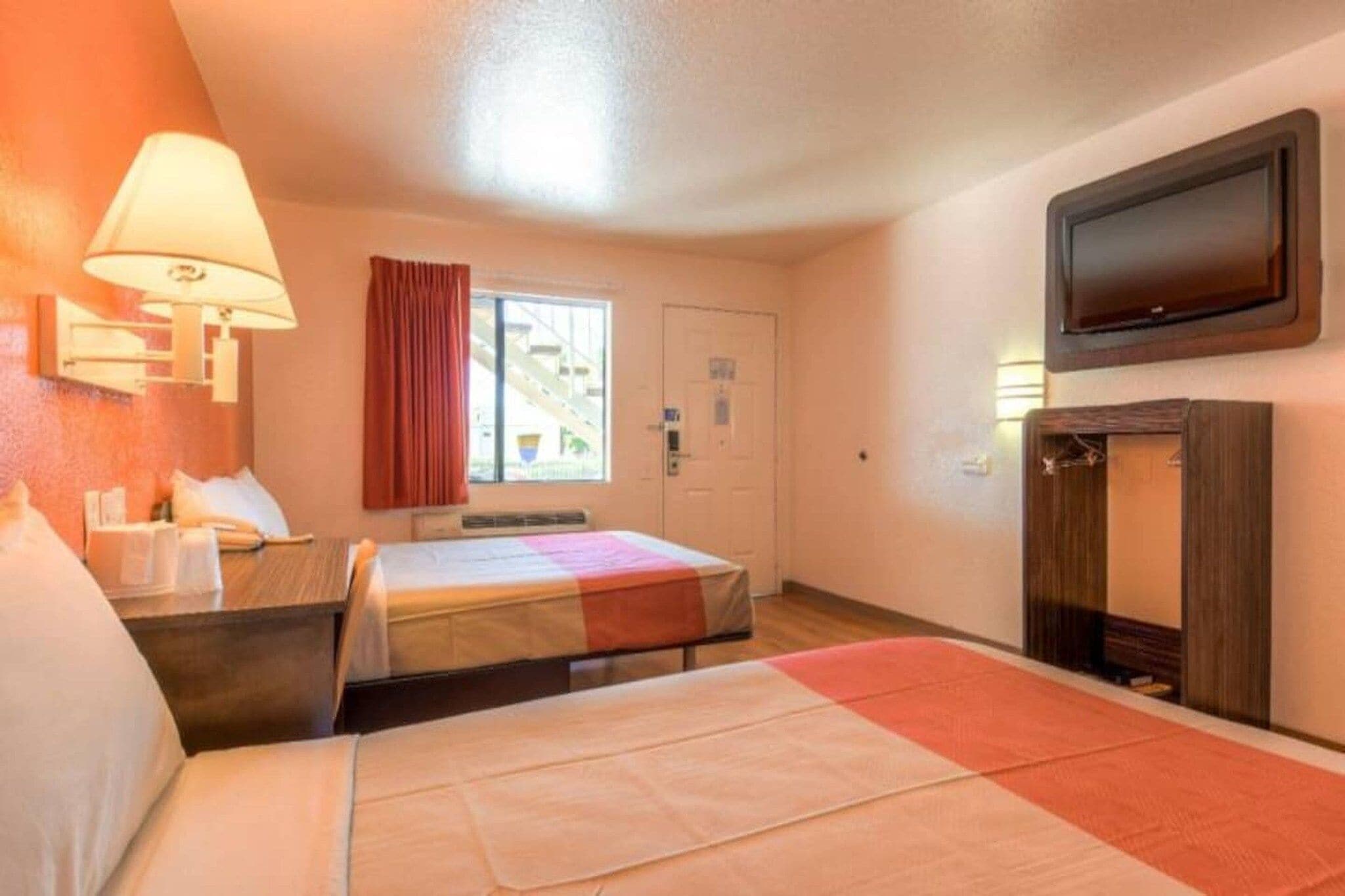 Ein Hotelzimmer mit einem Bett, einem Schreibtisch, einem Stuhl, einem Fernseher und einem Fenster mit Vorhängen.