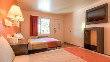Ein Hotelzimmer mit einem Bett, einem Schreibtisch, einem Stuhl, einem Fernseher und einem Fenster mit Vorhängen.