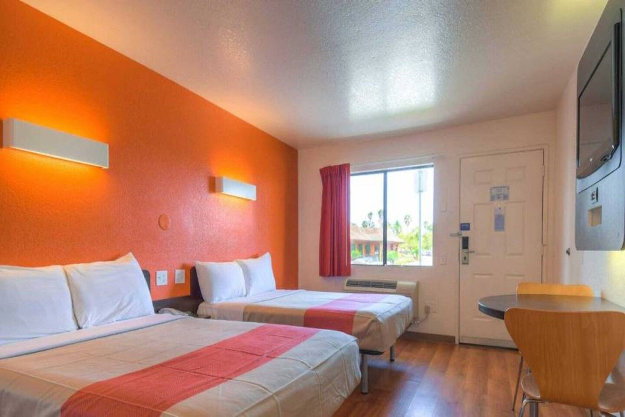 Una camera d'albergo con due letti, un tavolino, una sedia e una finestra con tende.