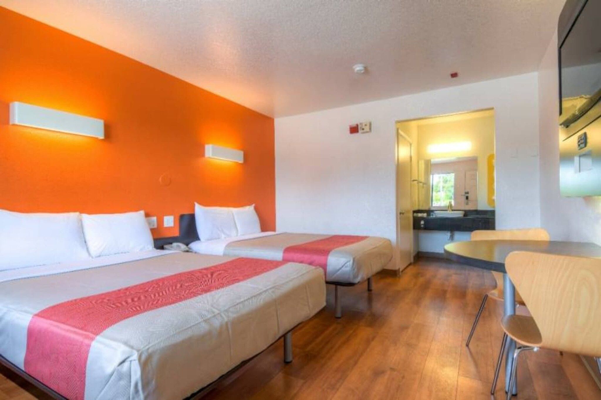A hotel room with two beds, a small table, and a chair.