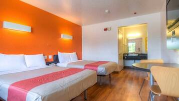 A hotel room with two beds, a small table, and a chair.