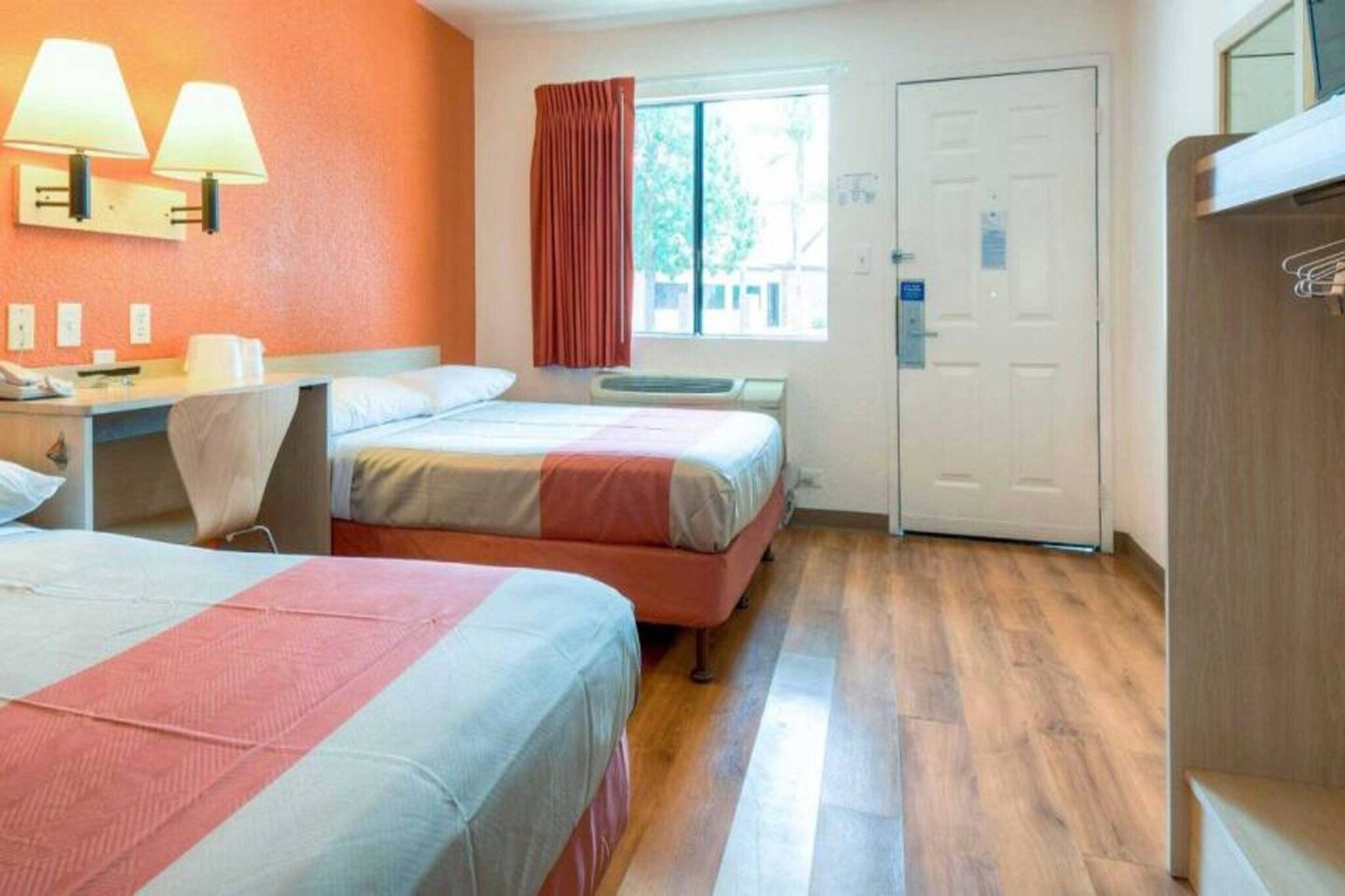 Une chambre d’hôtel avec deux lits, un bureau, une chaise, une fenêtre avec des rideaux et une porte.