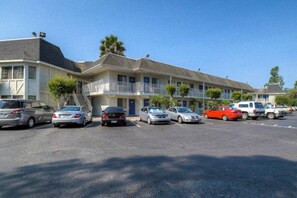 Un motel composé de plusieurs bâtiments à deux étages, un parking avec plusieurs voitures et un ciel bleu dégagé.