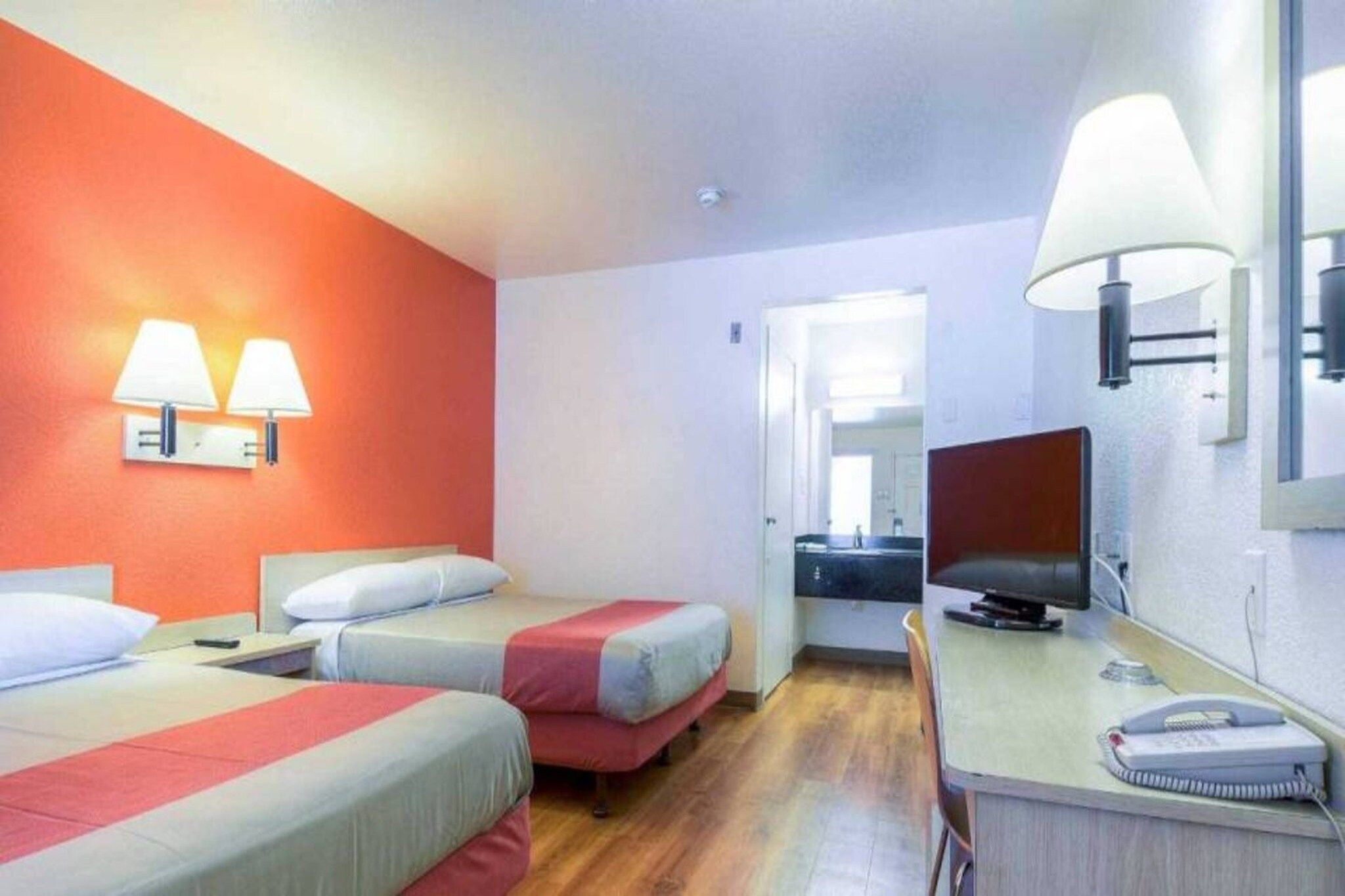 A hotel room with two beds, a desk, a chair, a television, and a telephone.