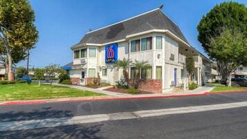 A two-story motel with a prominent '6' sign, a brick facade, and a red curb.