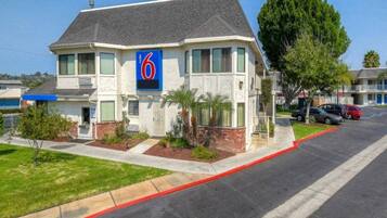 A two-story motel with a '6' sign, a parking lot, and a street view.