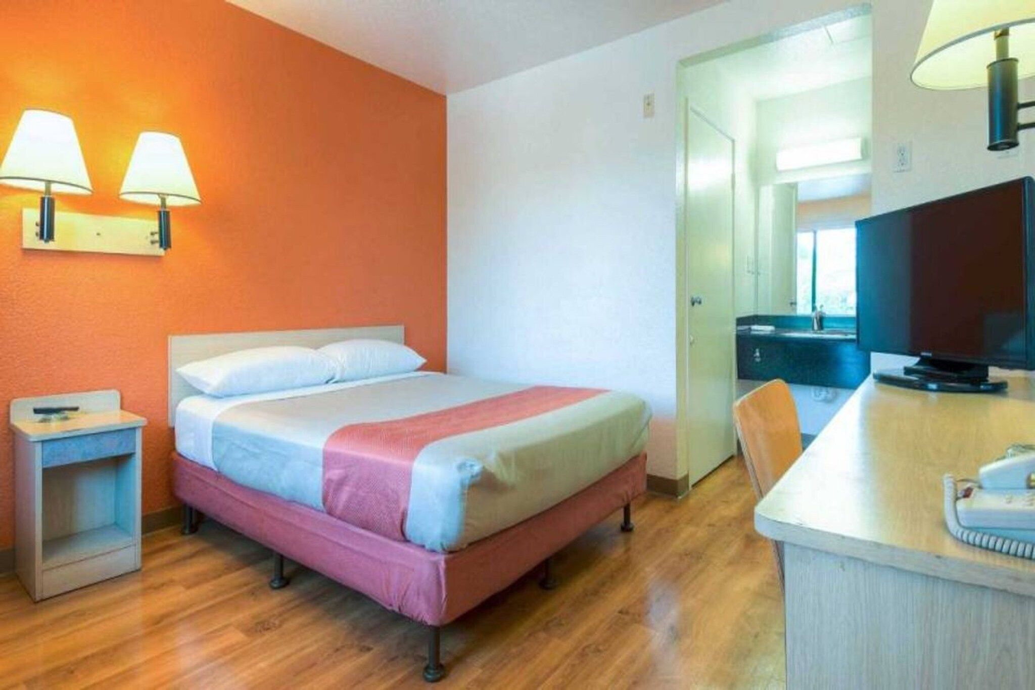 A hotel room with a bed, a desk, a chair, and a television.