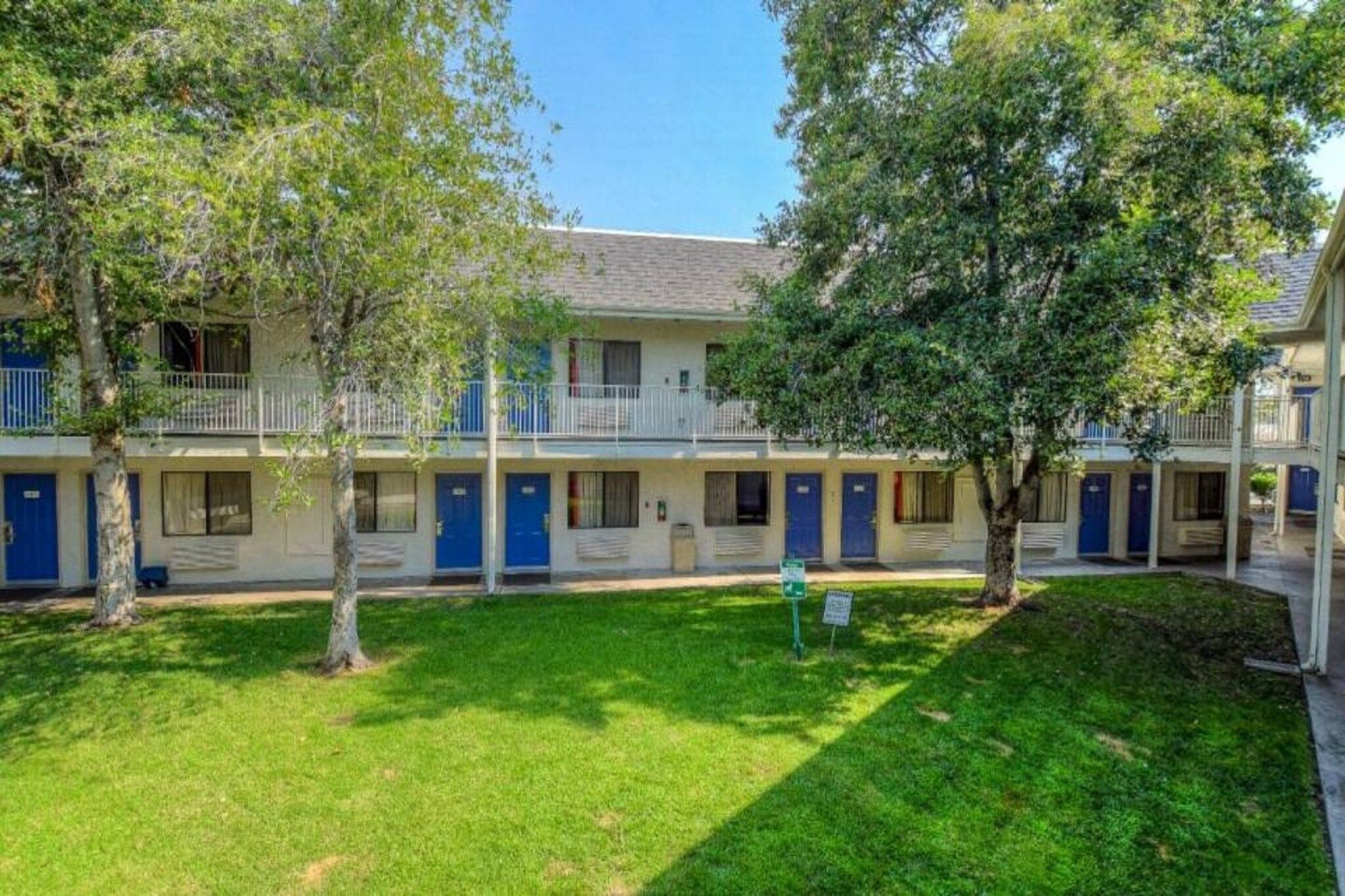 A row of motel buildings with blue doors and a grassy lawn in front.