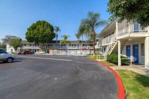 A motel with a parking lot, a row of rooms with balconies, and a clear sky. - Cozy ADA QueenBed|Pool|Free Parking (El Cajon)