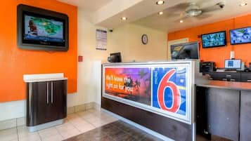 A reception area with a digital screen, a clock, and a counter with a sign.