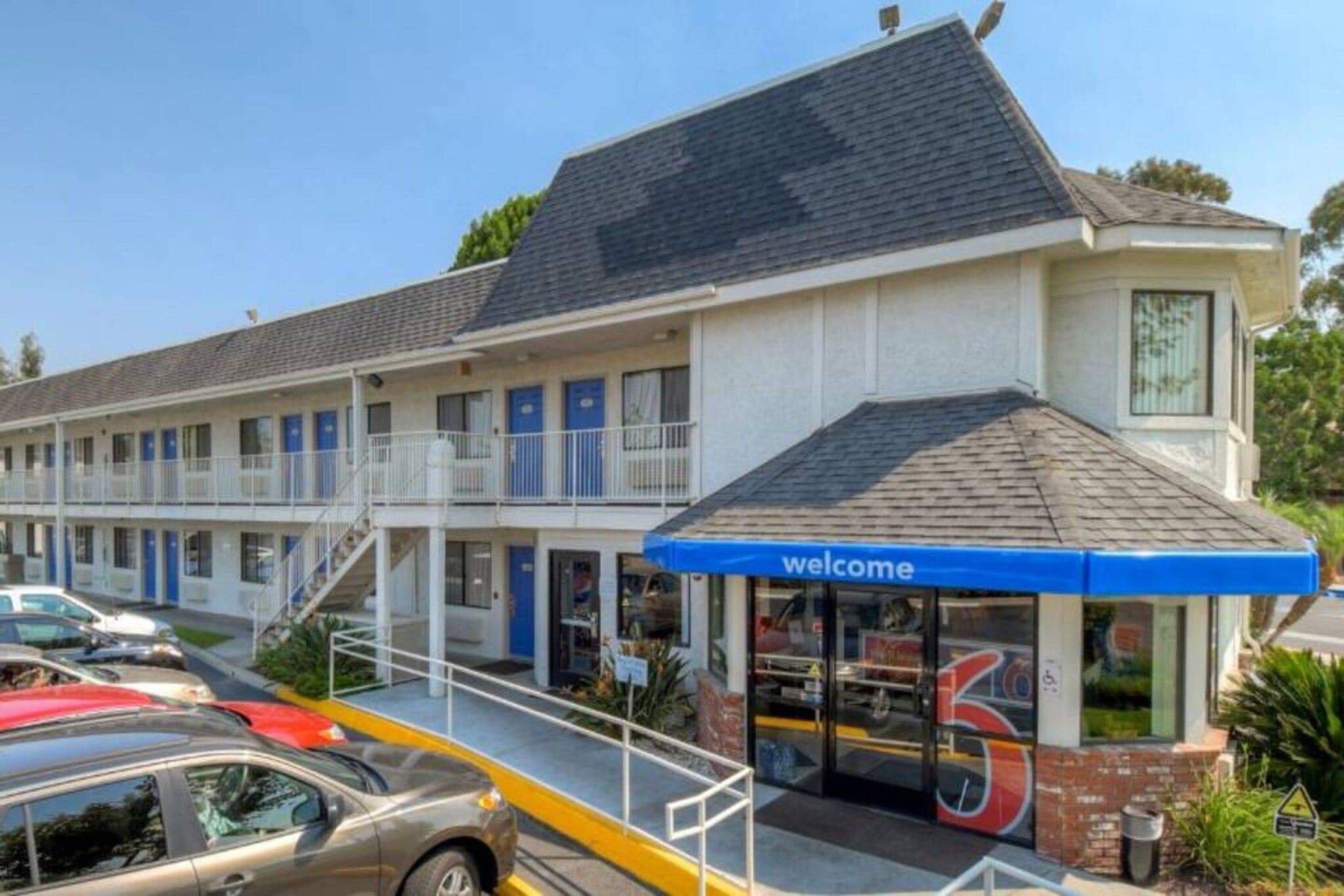 Un motel avec une enseigne « Bienvenue », une entrée abritée et un parking rempli de voitures.