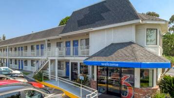 Un motel avec une enseigne « Bienvenue », une entrée abritée et un parking rempli de voitures.