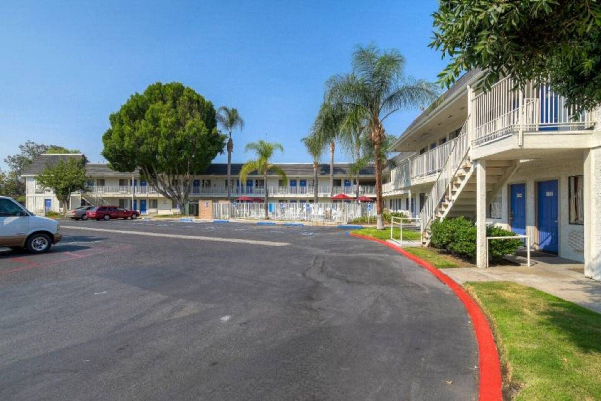 Un motel avec un parking, une rangée de chambres dotées de balcons et un ciel dégagé.