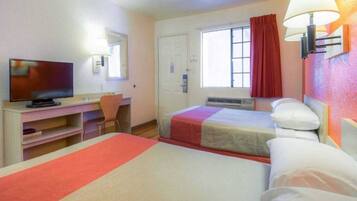 Une chambre d’hôtel avec deux lits, un bureau, une télévision et une fenêtre avec des rideaux.