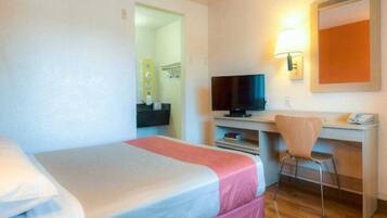 A hotel room with a bed, a desk with a computer, a chair, and a television.