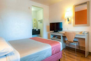 Una habitación de hotel con una cama, un escritorio con computadora, una silla y un televisor.