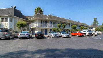A motel with multiple two-story buildings, a parking lot with several cars, and a clear blue sky.