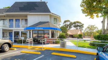 A hotel entrance with a 'welcome' sign, a covered waiting area, and a parking lot with yellow curbs.