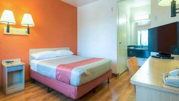 A hotel room with a bed, a desk, a chair, and a television.
